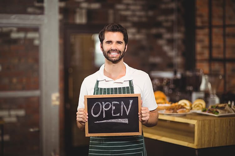 Smiling waiter showing chalkboard with open sign encouraging shopping local.